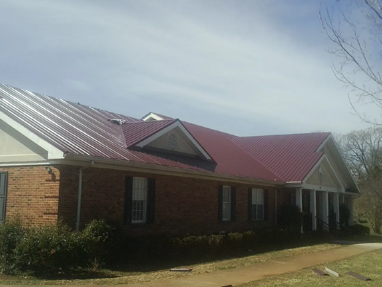 Red metal roof with gabled entries on a long brick building, from a Hail Damage Roof Repair job in Archie