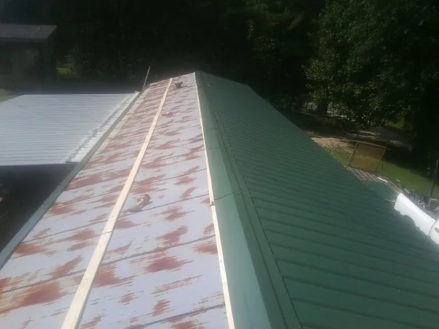 Old rusted panels beside newly installed green metal roofing — Wind Damage Roof Repair by Roofing Brothers in Archie