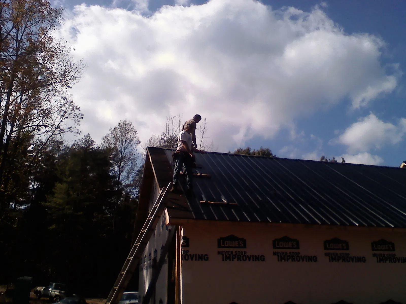 Roofer fastening dark metal panels high against a cloudy sky, from a Roof Inspection job in Archie