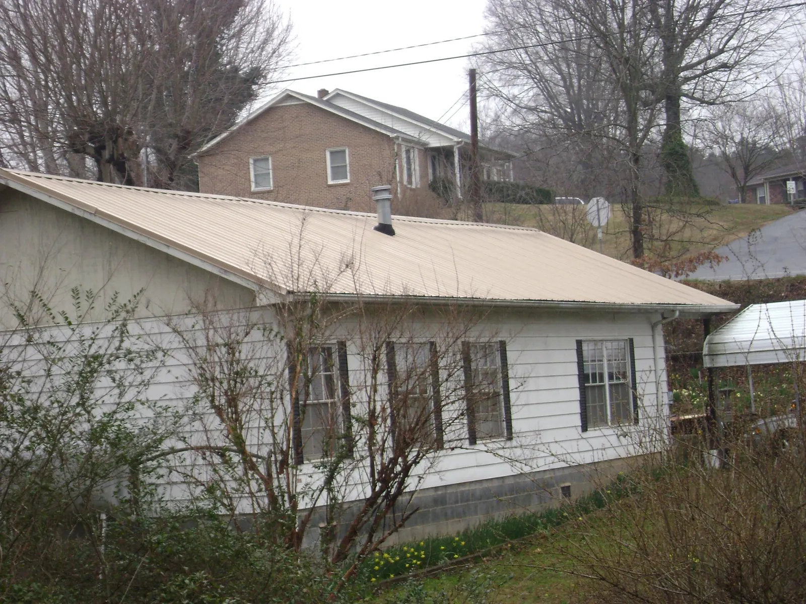 Tan metal roof on a white sided house set into a hillside — Commercial Roofing by Roofing Brothers in Archie